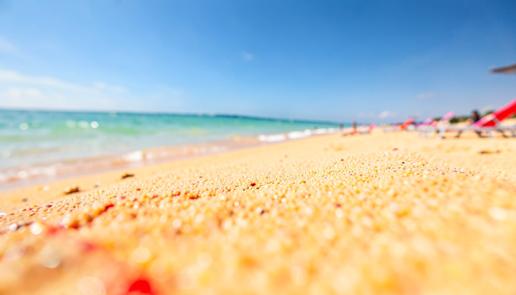 Wide-angle view of a golden sandy beach with turquoise shallow water stretching to the horizon under a bright blue sky